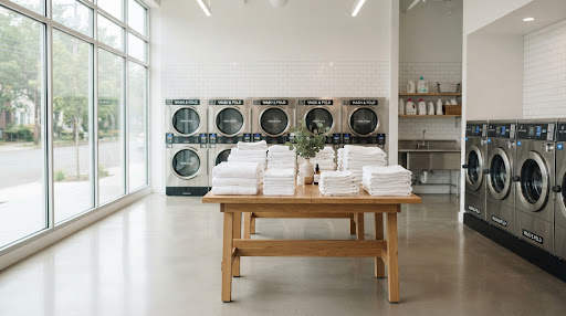 Interior gerai laundry bersih wangi dengan jajaran mesin cuci modern dan tumpukan handuk rapi di atas meja kayu